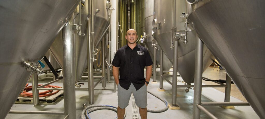 Man standing in front of beer brewing machinery.